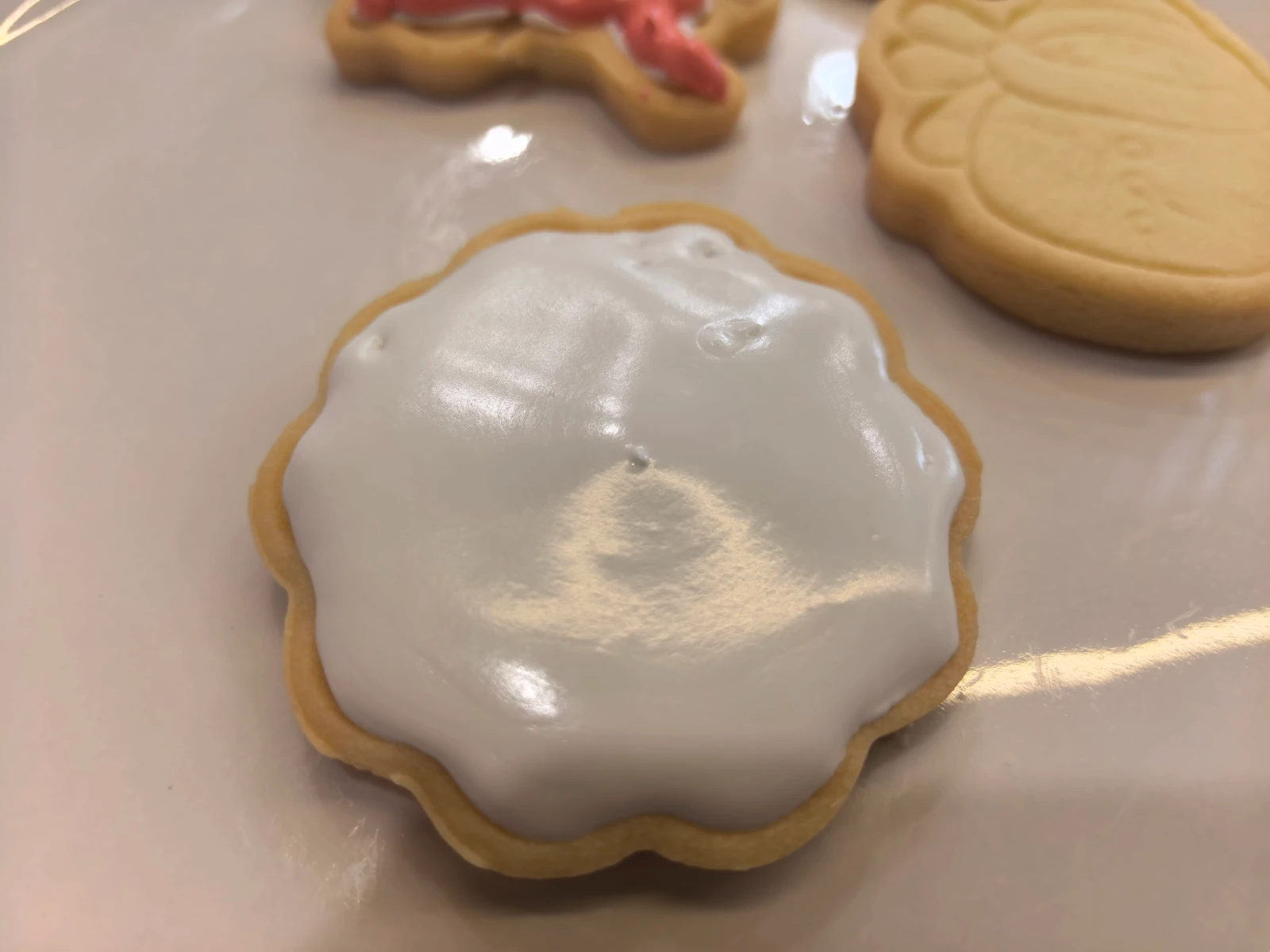 A close-up source photograph of a scalloped cookie with glossy white icing on a warm-toned surface.